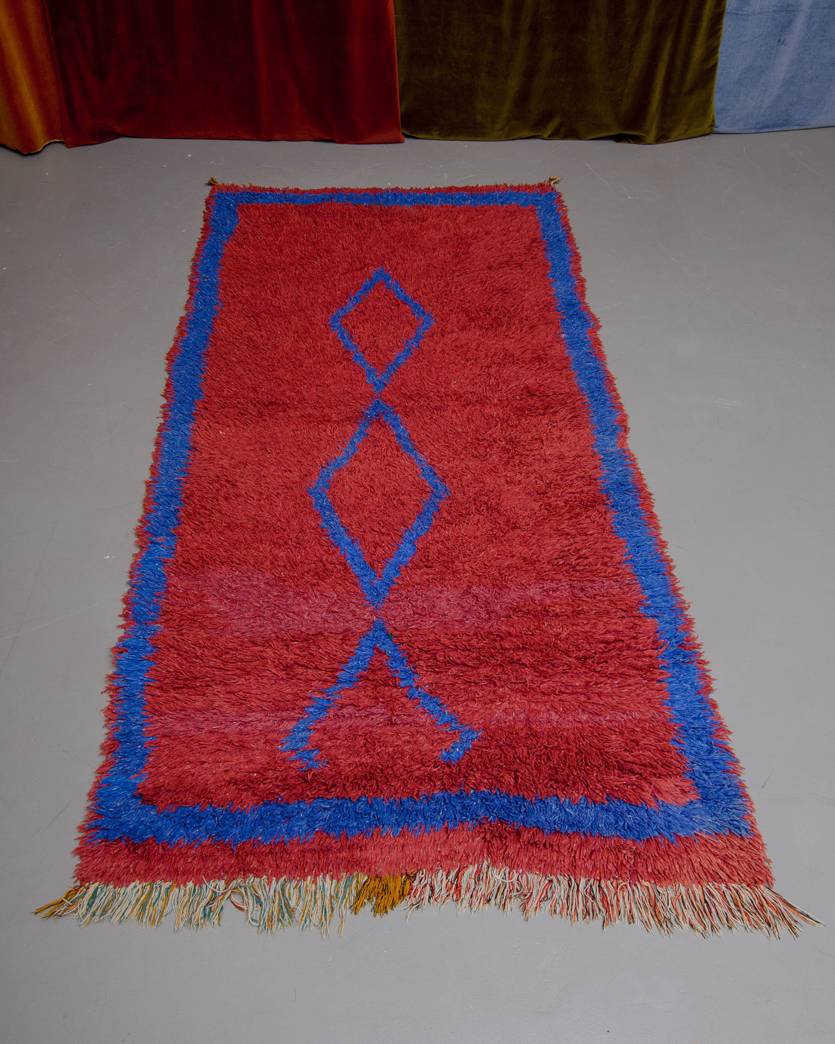 Vintage Berberlin boucherouite runner rug on grey floor in front of velvet curtain. 