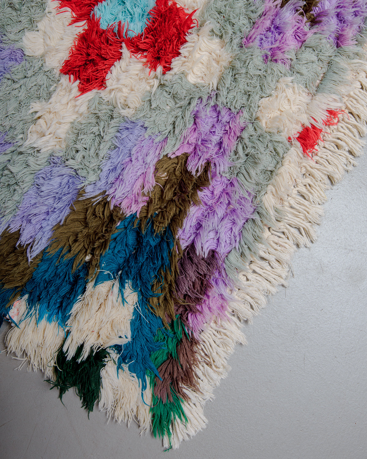 Corner of boucherouite rug with red, green, orange, blue and white cotton.