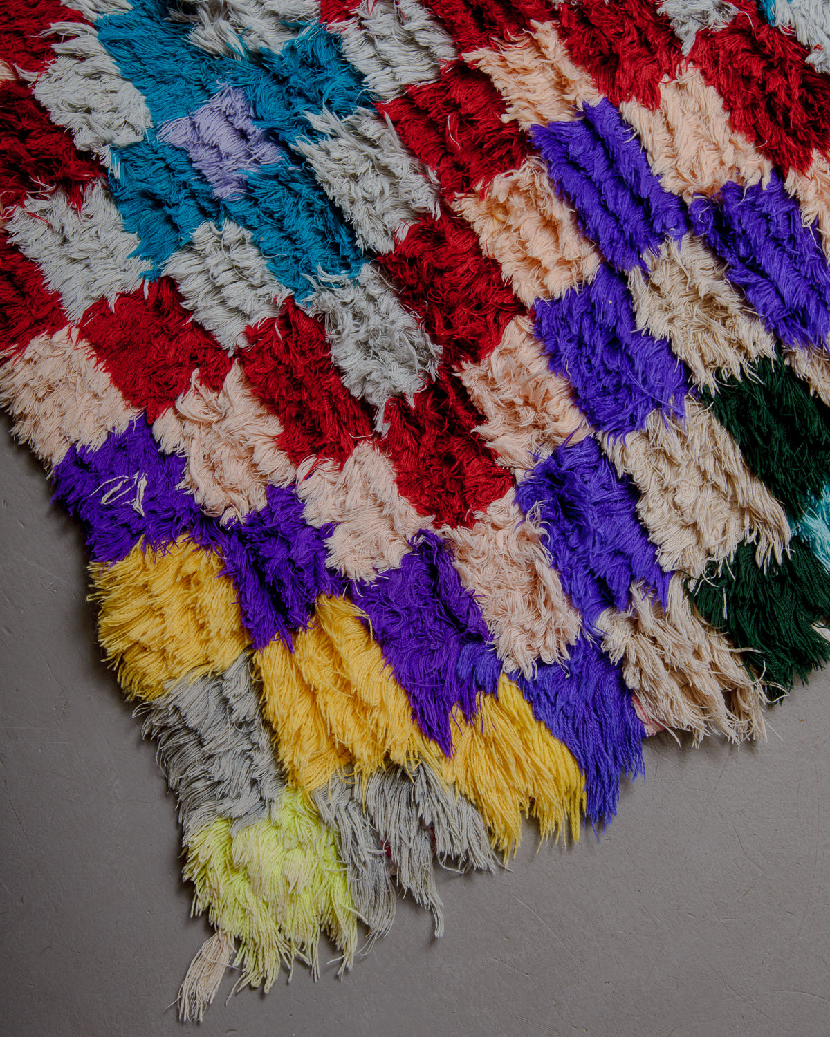 Corner of boucherouite rug with red, green, orange, blue and white cotton.