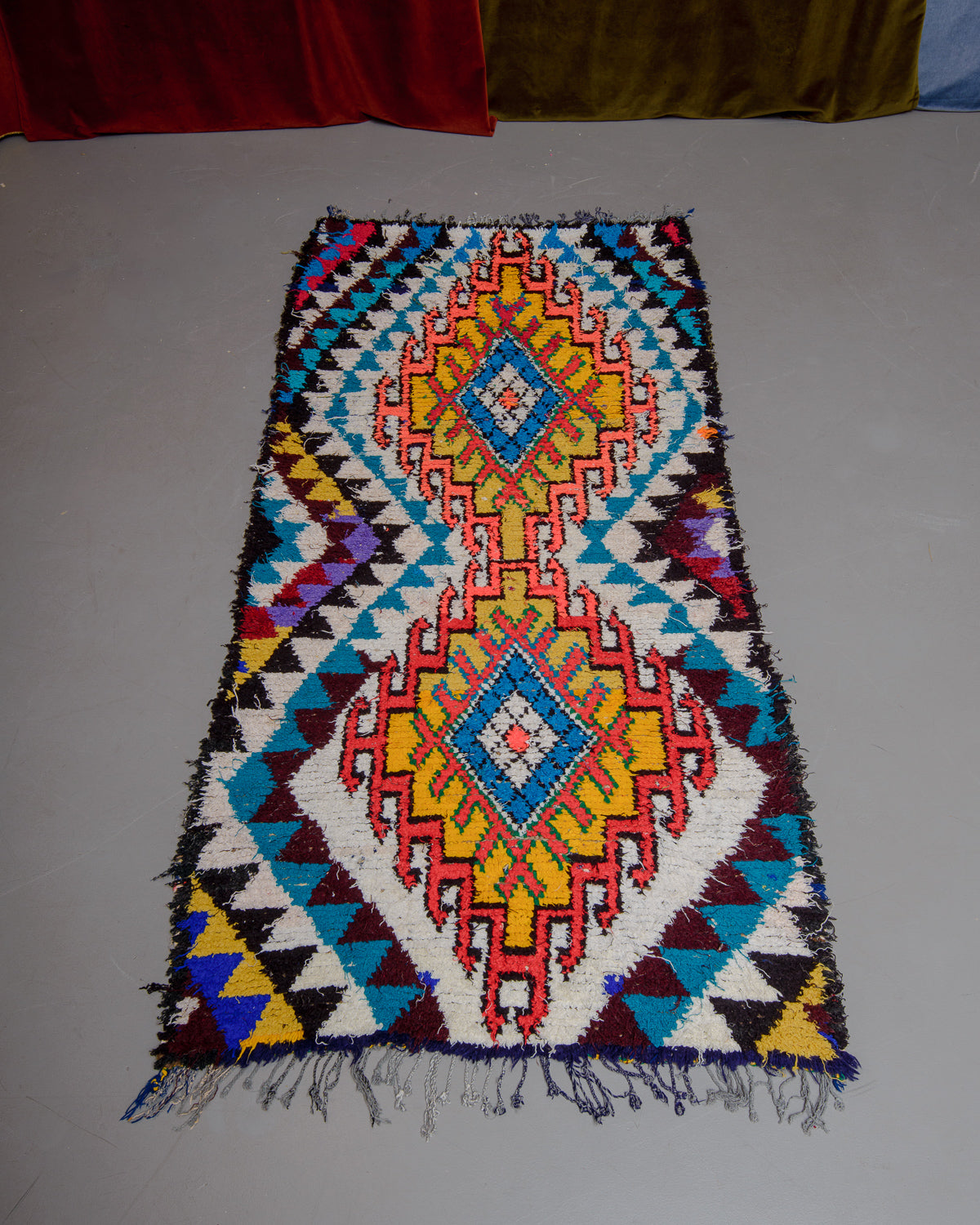 Vintage Berberlin boucherouite runner rug on grey floor in front of velvet curtain. 