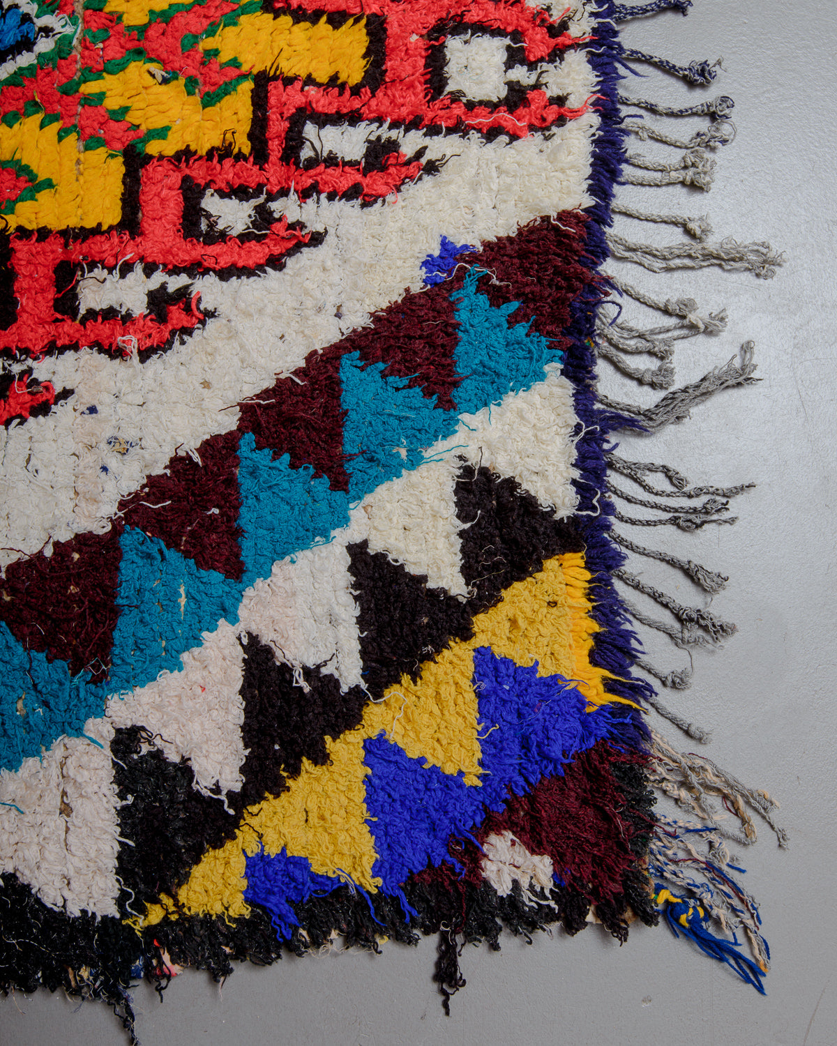 Corner of boucherouite runner rug with tassels on grey floor.