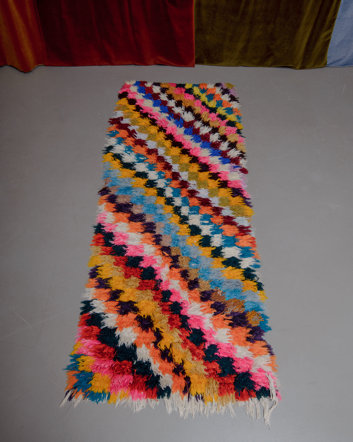 Vintage Berberlin boucherouite runner rug on grey floor in front of velvet curtain. 