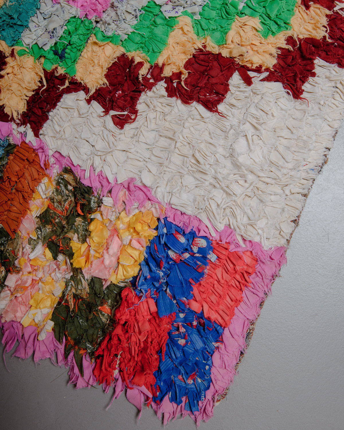 Corner of colourful boucherouite rug on a grey floor.