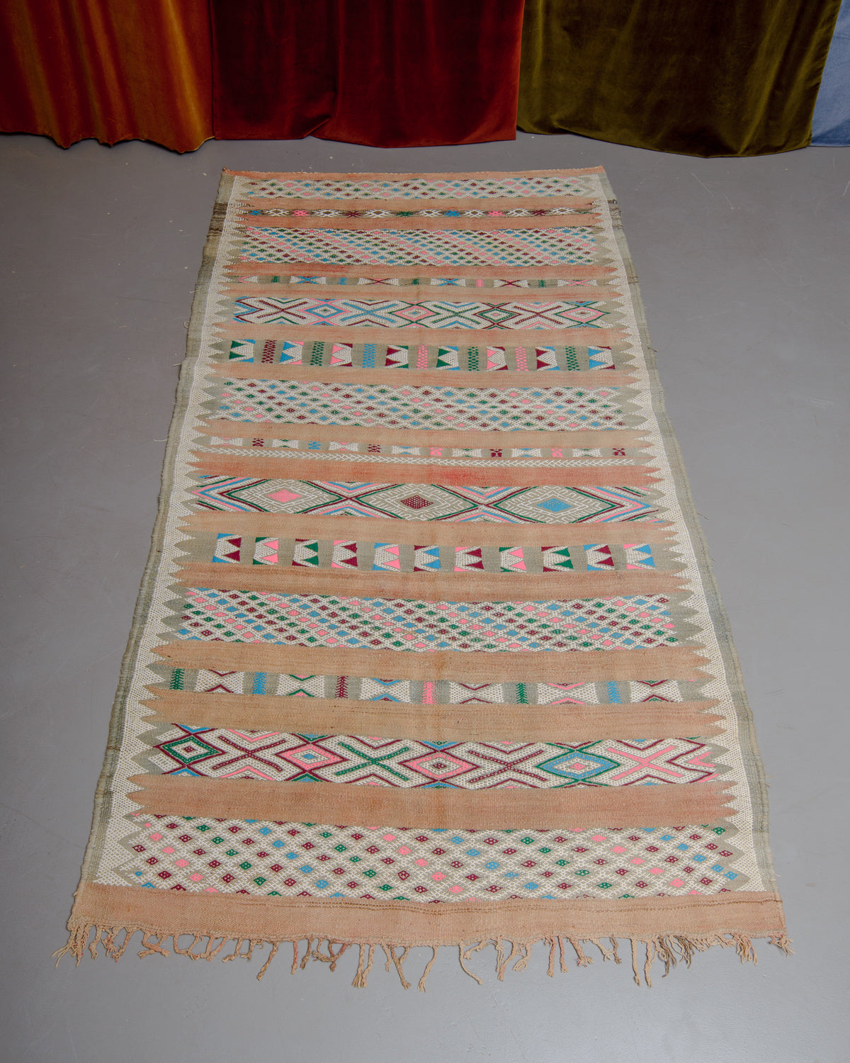Vintage Kelim rug in muted shades of beige, rose, green, blue and pink on grey floor.