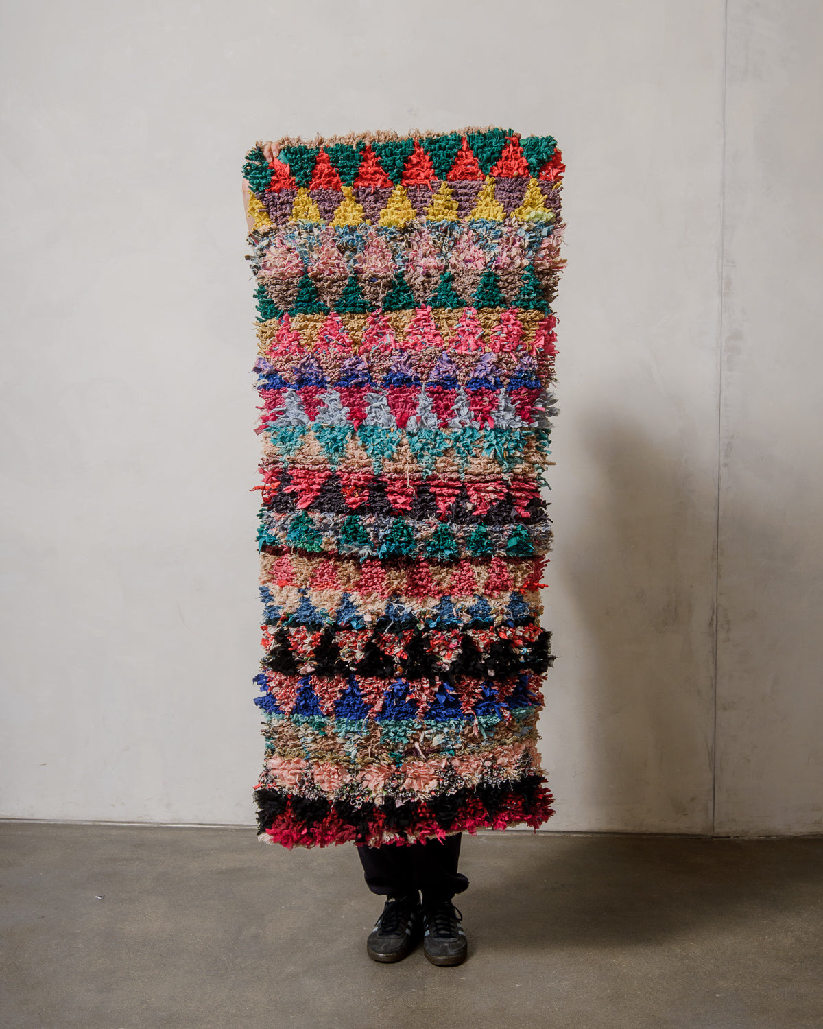 Berberlin boucherouite runner rug held in front of a plain wall. 