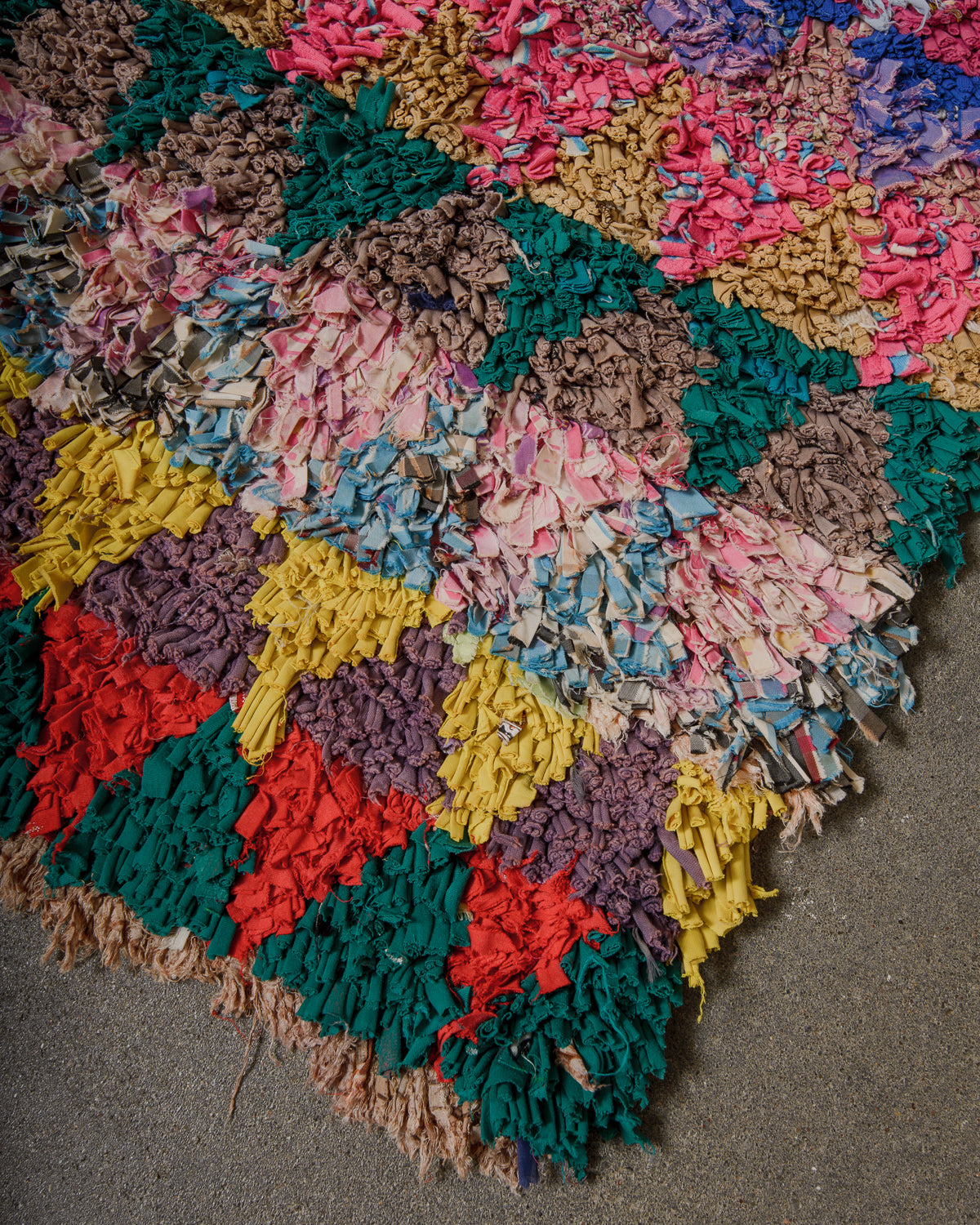 Corner of rag rug on cement floor with lots of colours. 