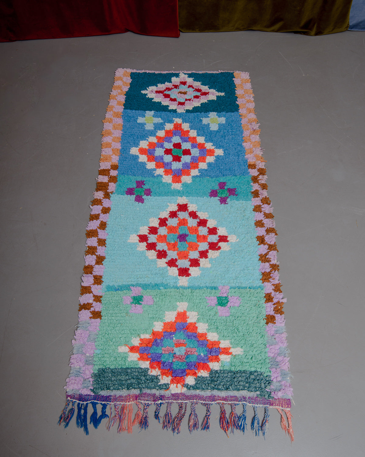 Vintage Berberlin boucherouite runner rug on grey floor in front of velvet curtain. 