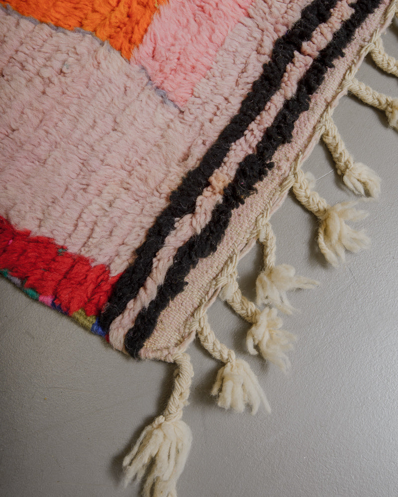 Corner of rug with black stripes along the bottom and natural wool tassels. 