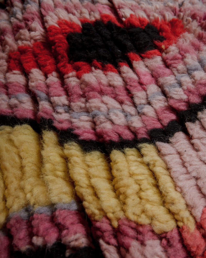 Close up of wool rug with pink, red, butter yellow and black.