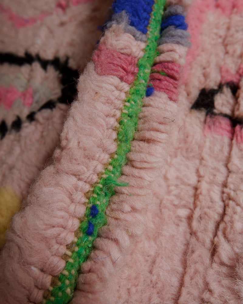 Close up of wool rug showing pink pile and green weft.