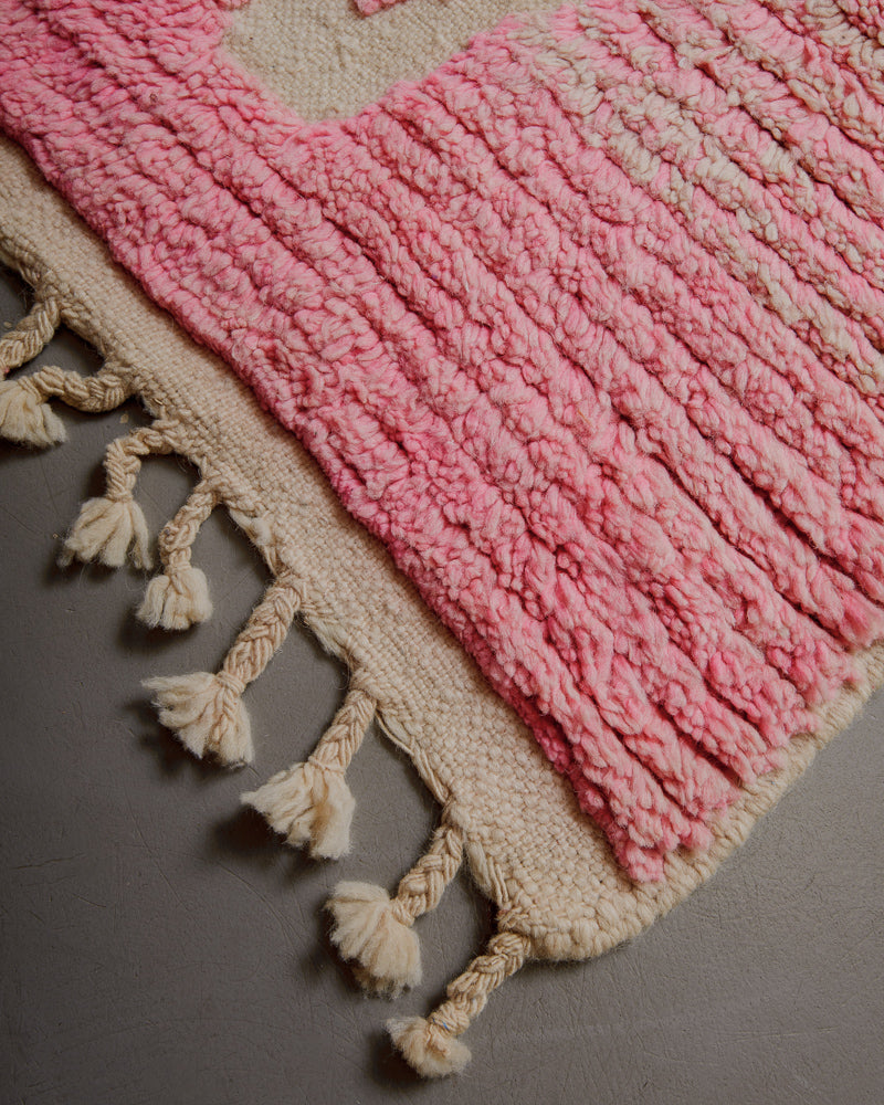 Corner of wool rug with natural wool tassels on grey floor. 