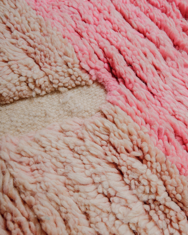 Surface of wool rug in shades of pink with plush pile and woven areas. 