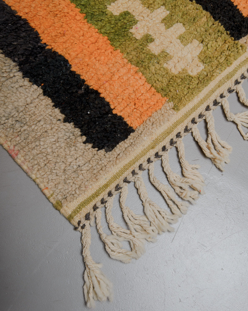 Corner of wool rug with natural wool tassels on grey floor. 