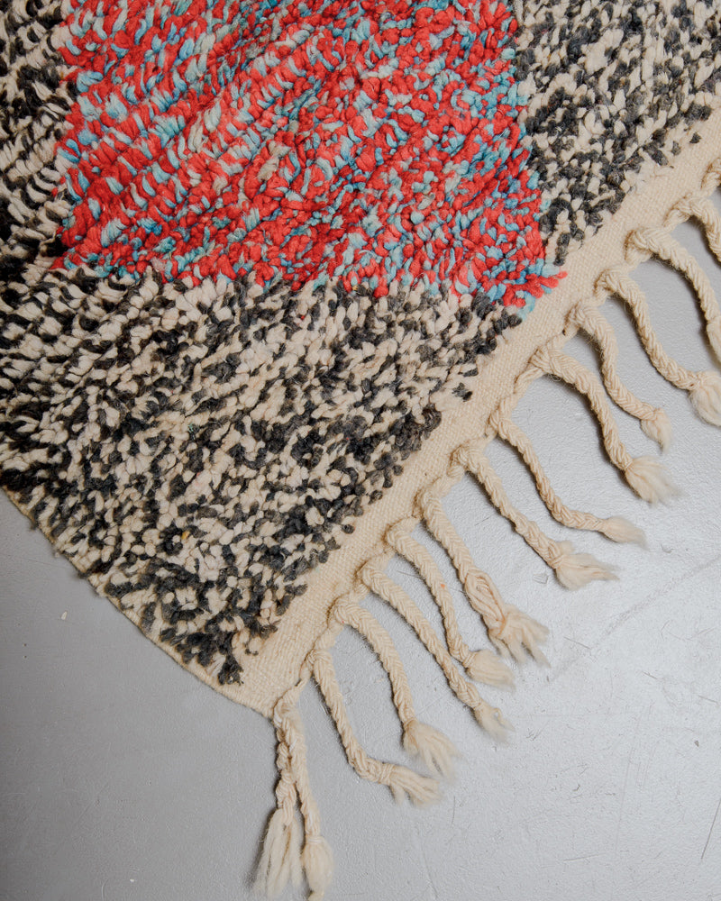 Corner of wool rug with natural wool tassels on grey floor. 