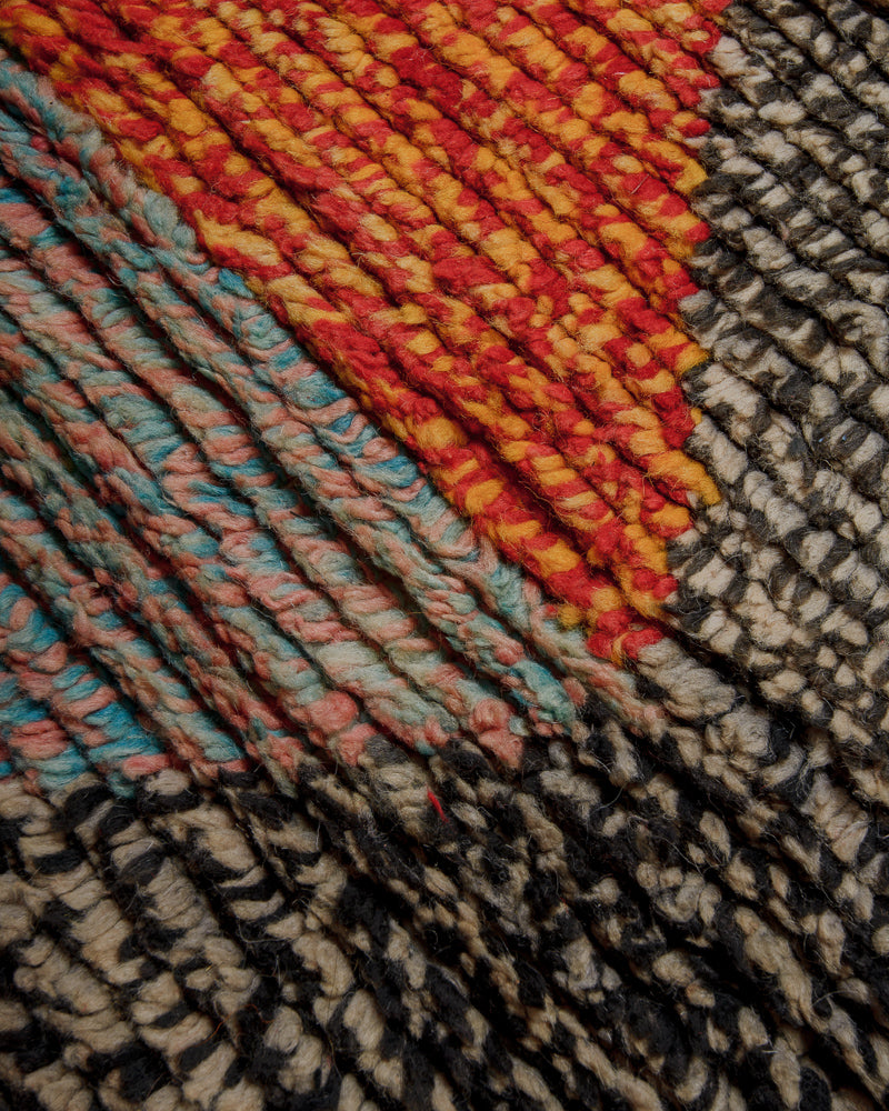 Surface of vintage wool rug speckled colours in shades of black and white, red and yellow and blue and pink.