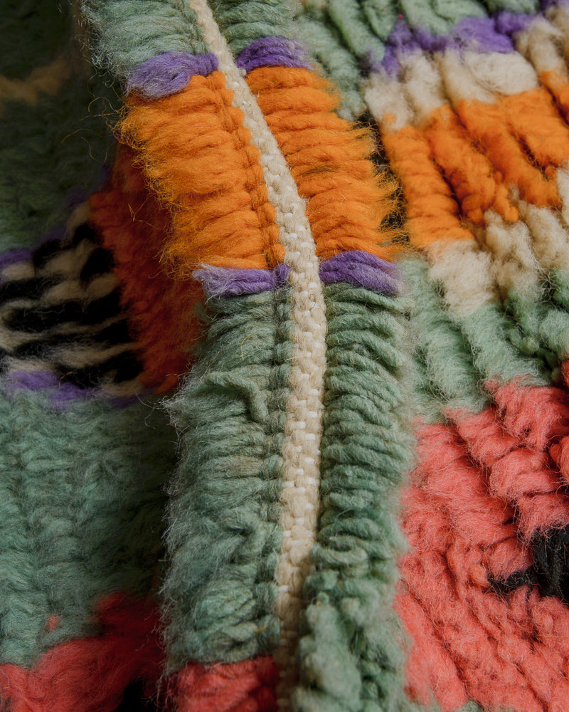 Close up of wool rug made of shades of turquoise, orange, purple and coral.