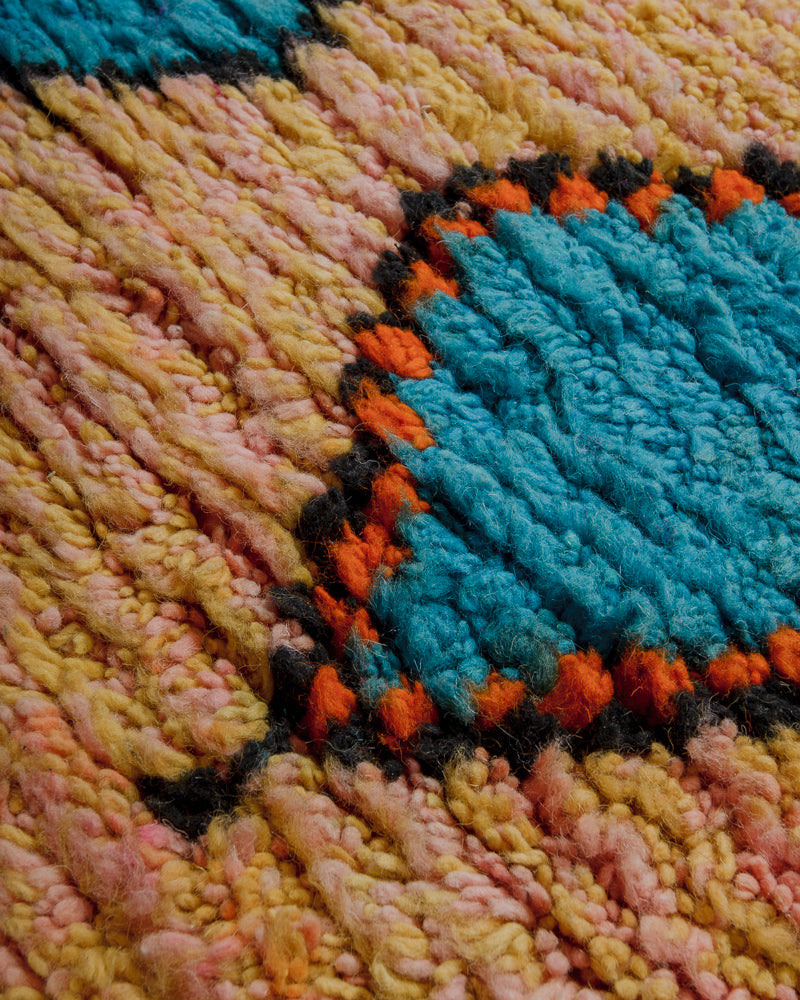 Surface of vintage wool rug showing the pink and yellow base colours. 