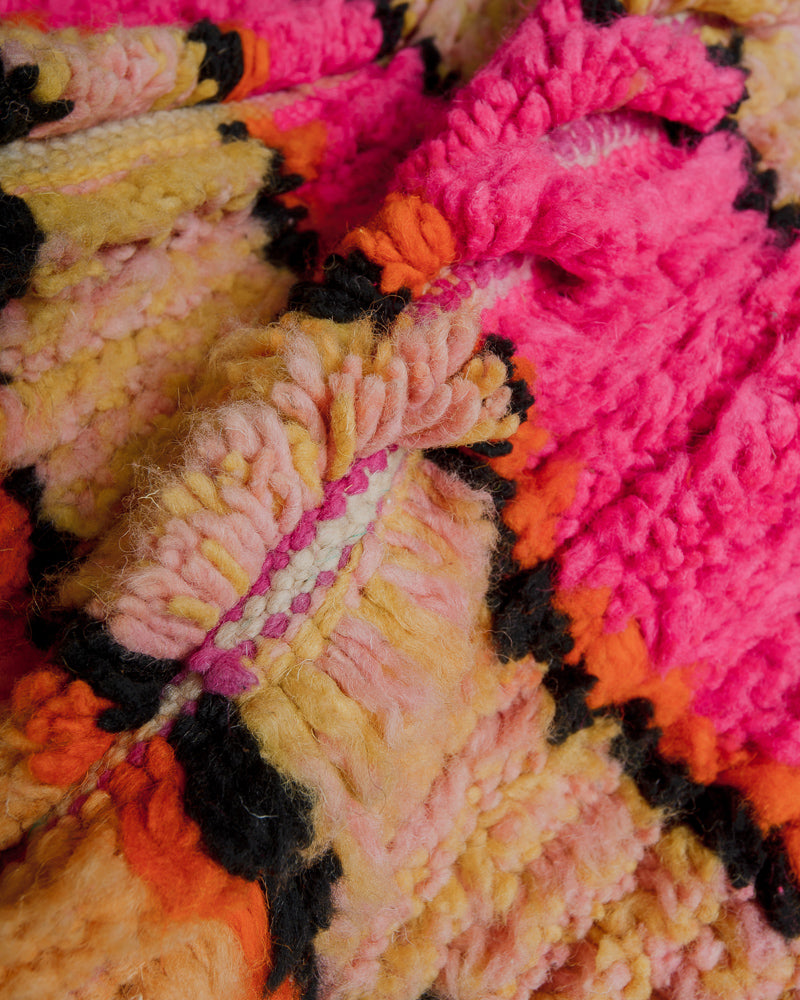 Close up of wool rug made of different shades of pink, yellow, orange and black.