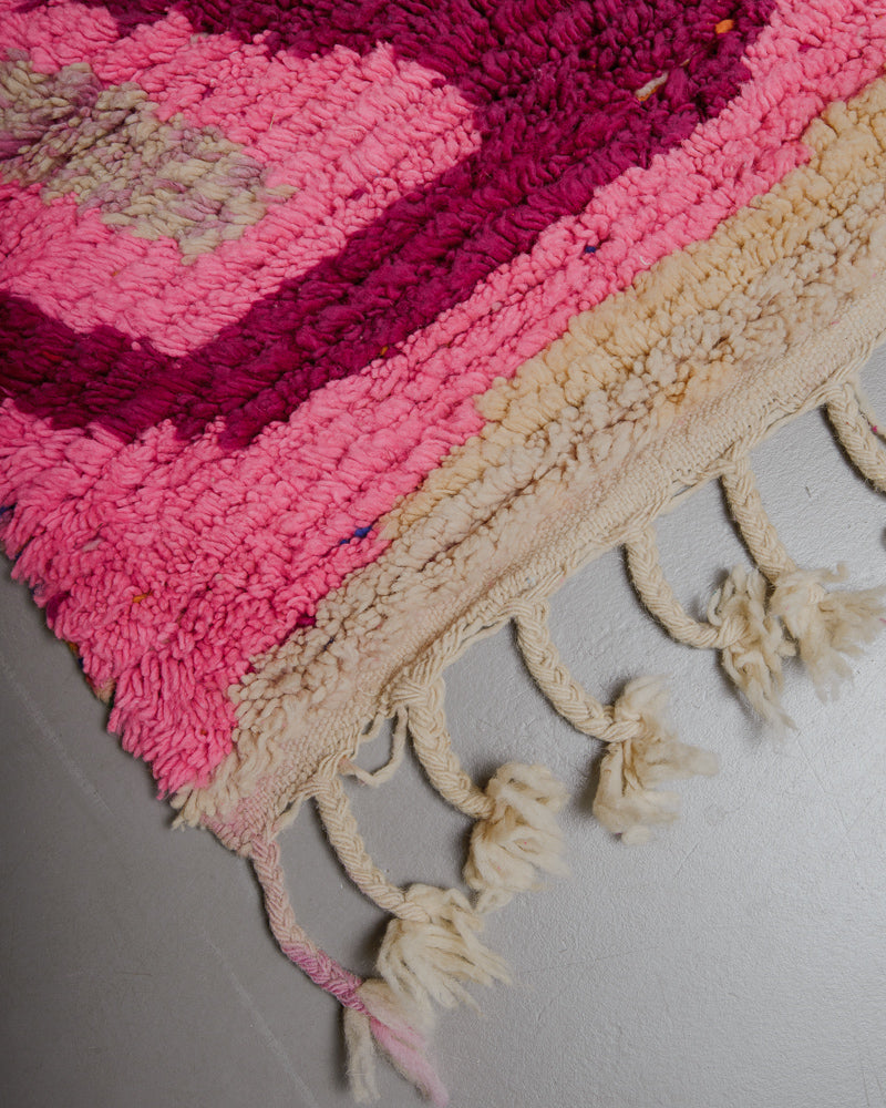 Corner of pink, red and cream wool rug with natural wool tassels. 