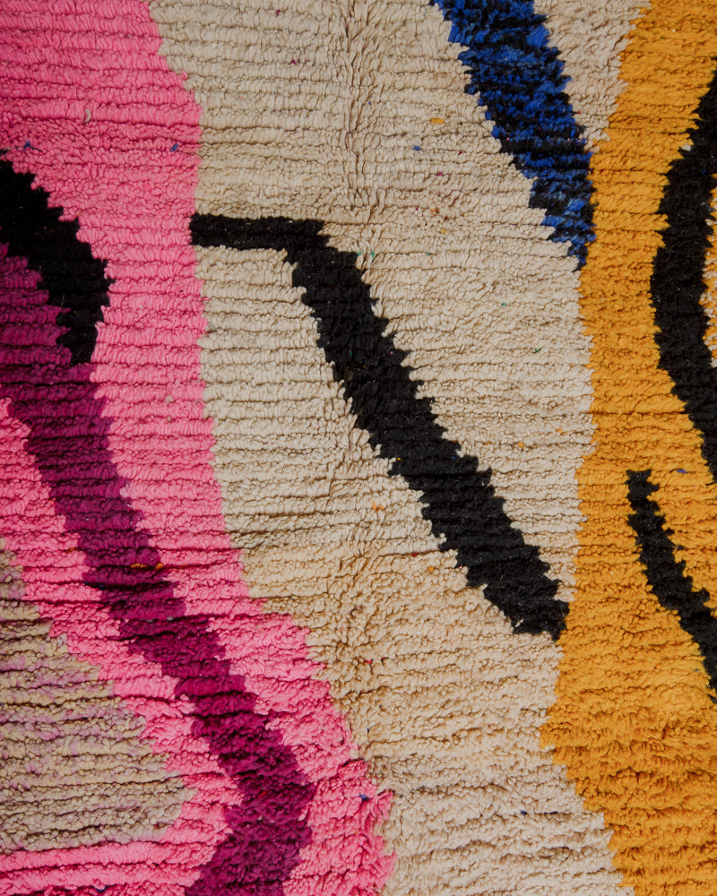 Close up of surface of wool rug with bold pink, yellow and black.