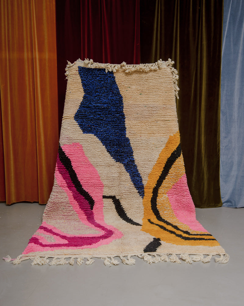 Berberlin Boujaad rug with bold forms and a soft rose coloured base held in front of velvet curtains.