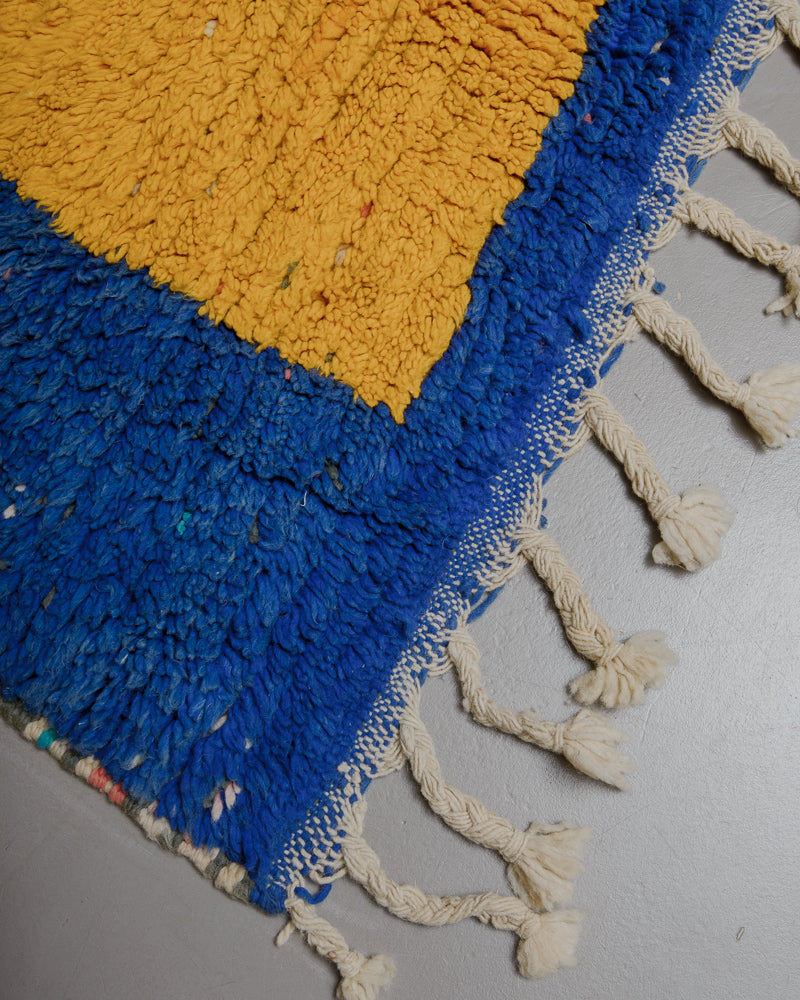 Corner of blue and yellow wool rug with natural wool tassels. 