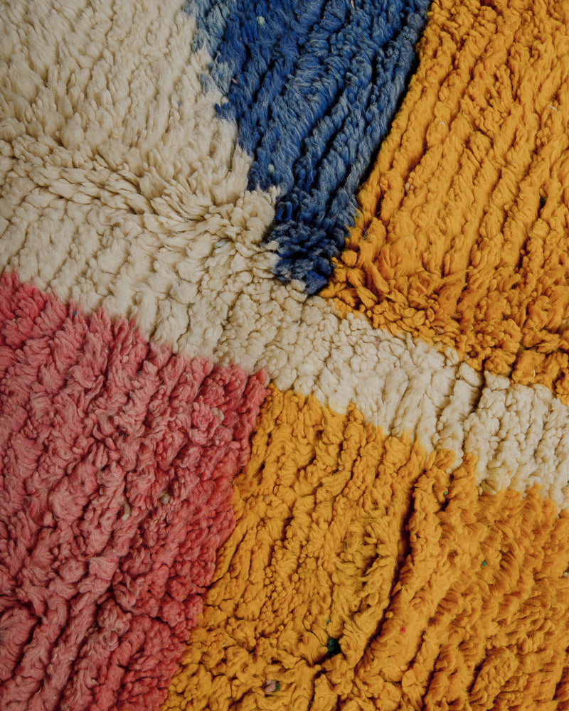 Surface of wool rug in yellow, creamy white, blue and pink.
