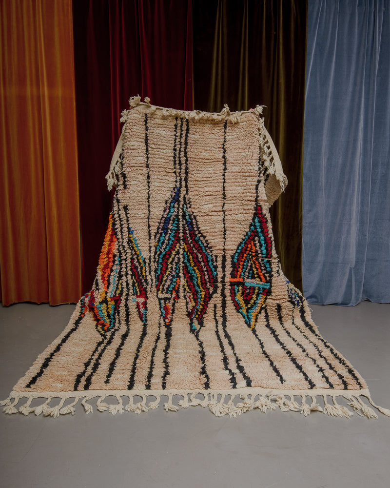 Vintage Boujaad rug in subtle salmon shade being held in front of a velvet curtain.