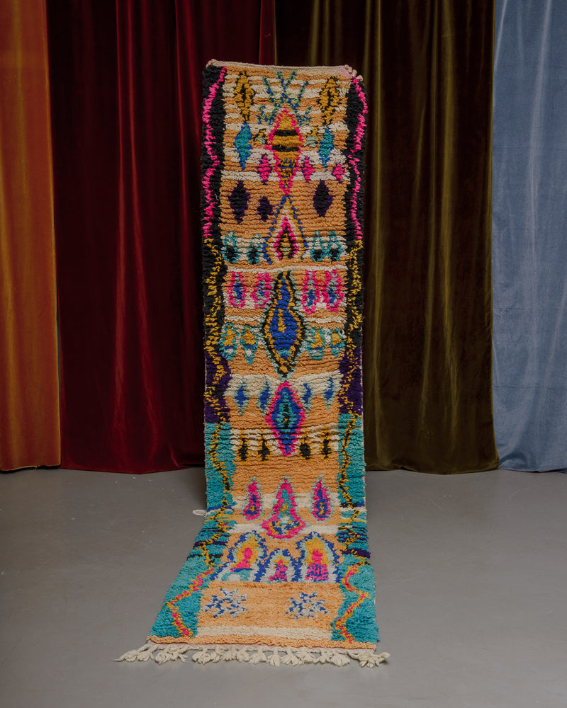 Vintage Berberlin runner rug being held up in front of a velvet curtain. 