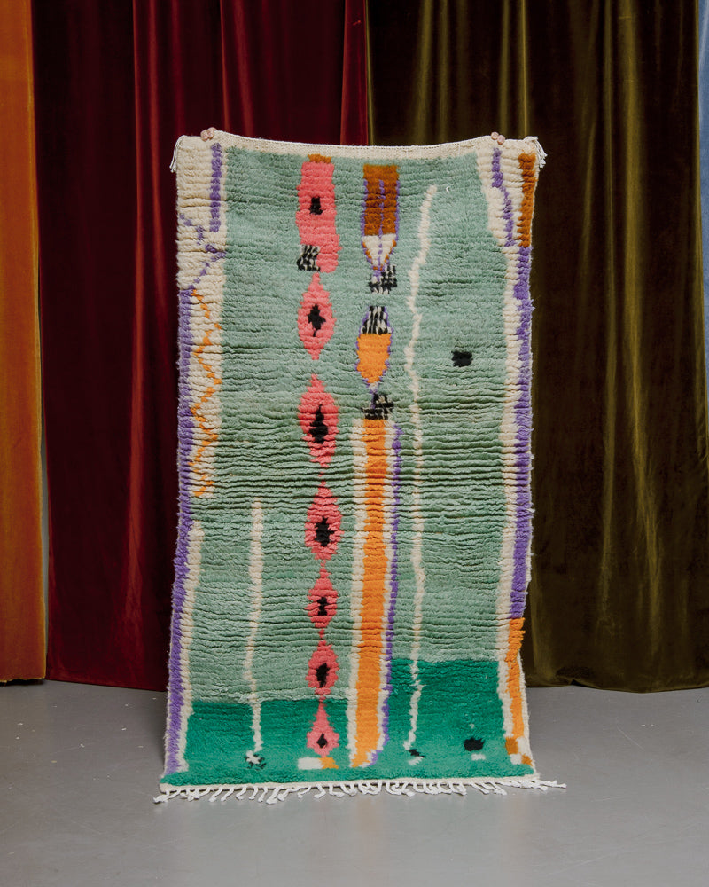 Vintage Berberlin runner rug being held up in front of a velvet curtain. 