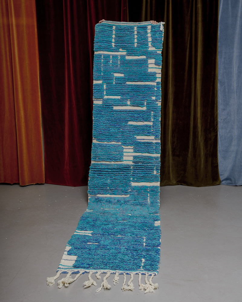 Vintage Berberlin runner rug being held up in front of a velvet curtain. 