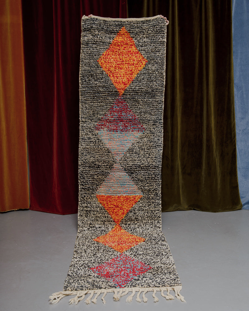 Vintage Berberlin runner rug being held up in front of a velvet curtain. 