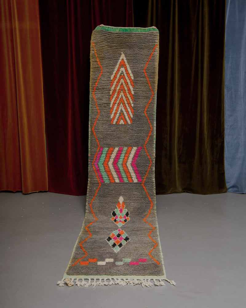 Vintage Berberlin runner rug being held up in front of a velvet curtain. 