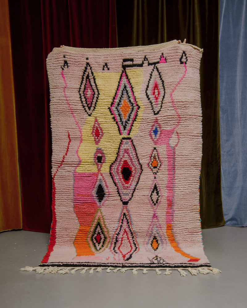 Vintage Boujaad rug made of pink, orange and yellow tones being held in front of a velvet curtain.