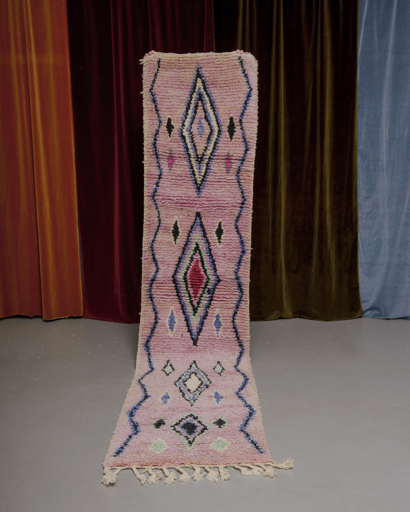 Vintage Berberlin runner rug being held up in front of a velvet curtain. 
