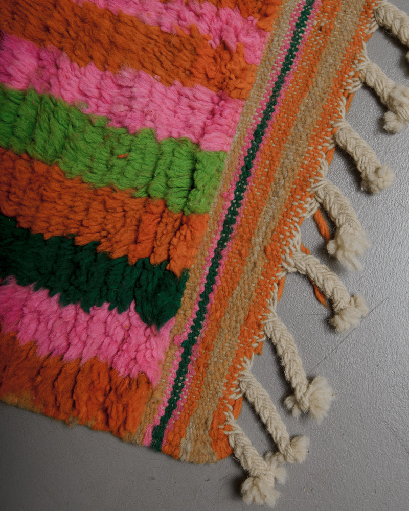 Corner of rug with colourful, striped woven edge and natural wool tassels. 