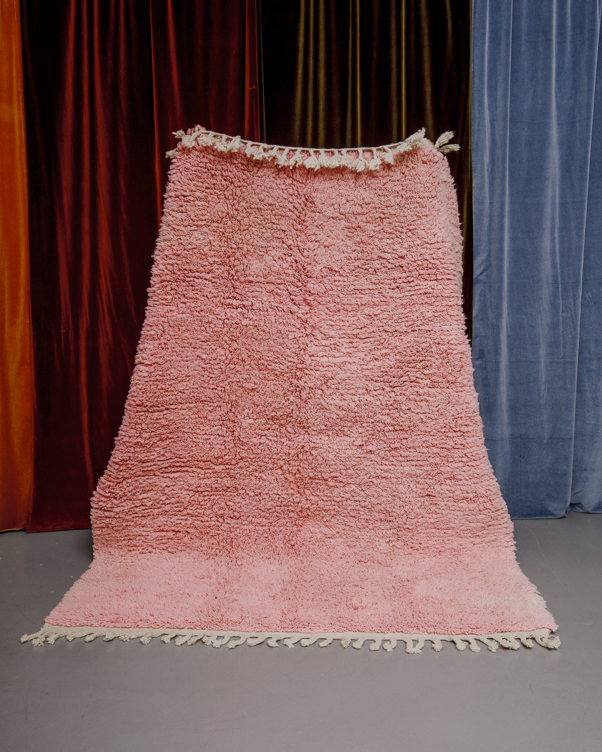 Berberlin Boujaad rug in soft rose being held in front of velvet curtains.