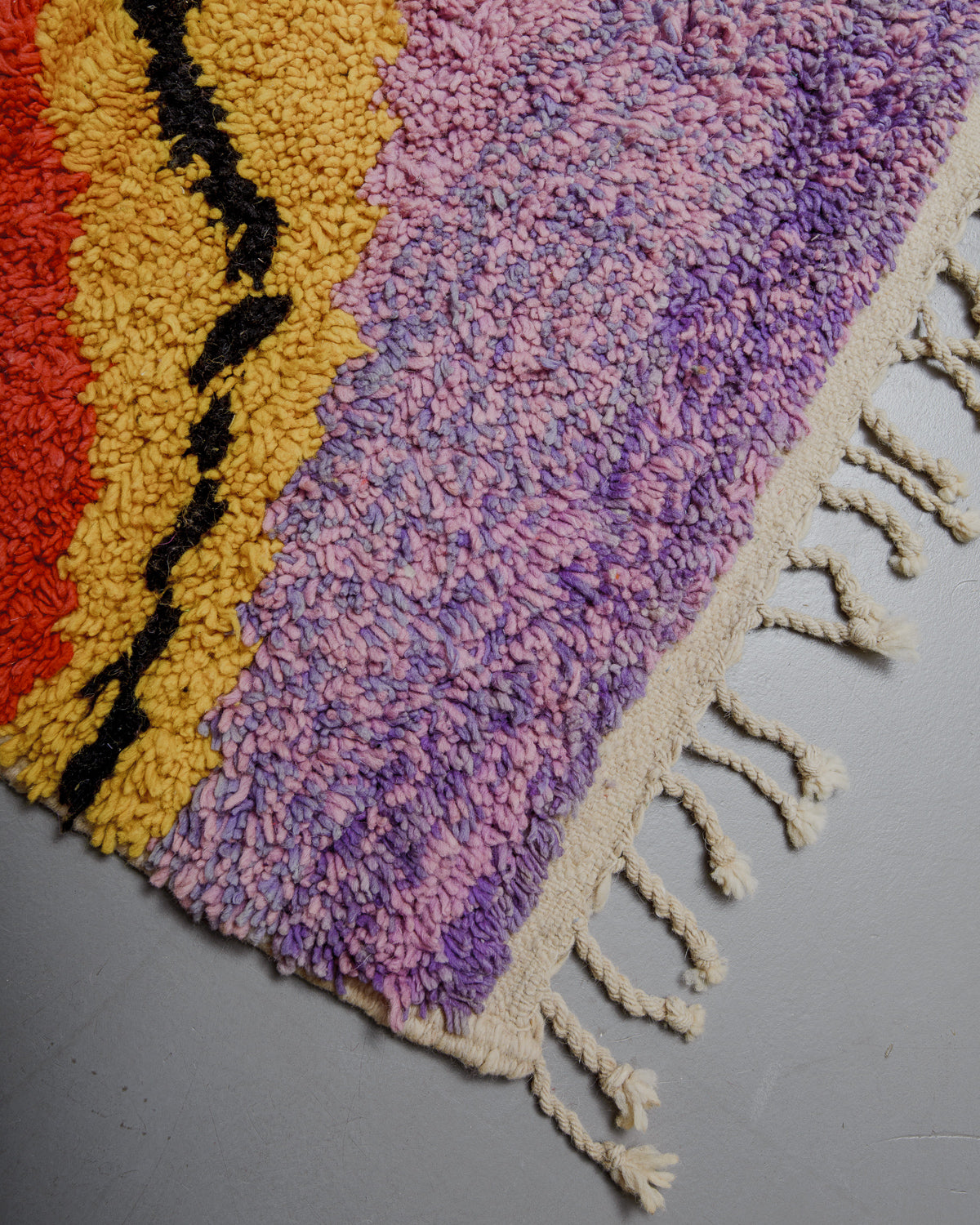 Corner of wool rug with flat woven edge with natural wool tassels. 