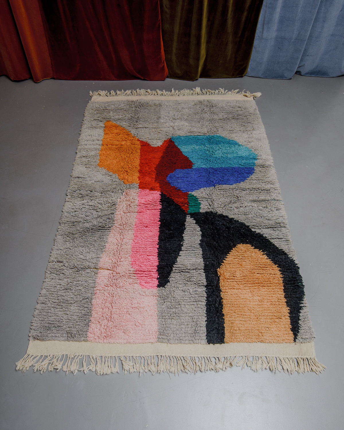 Berberlin Boujaad rug with bold forms in orange, red, blue, pink and grey on a grey floor. 