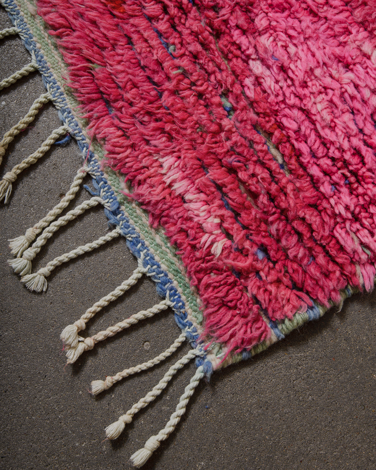 Close-up of a pink textured rug with tassels on a dark surface