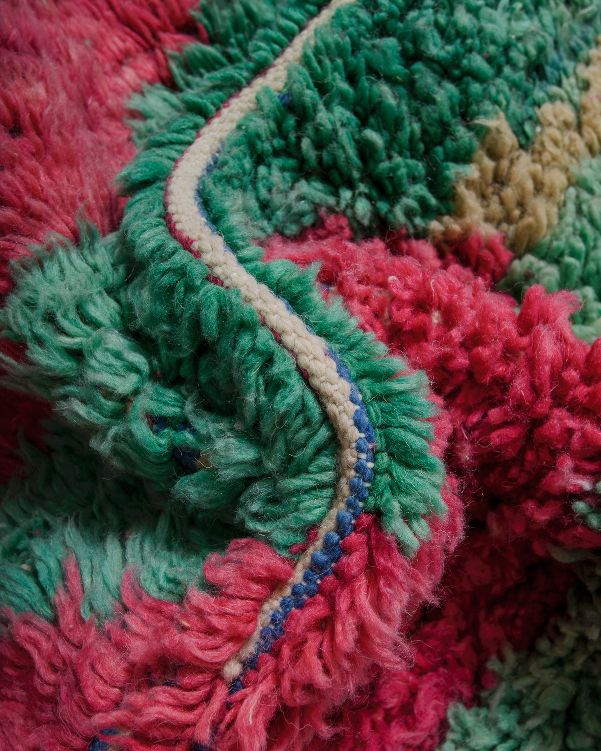 Close-up of a textured wool rug with pink and green colours.