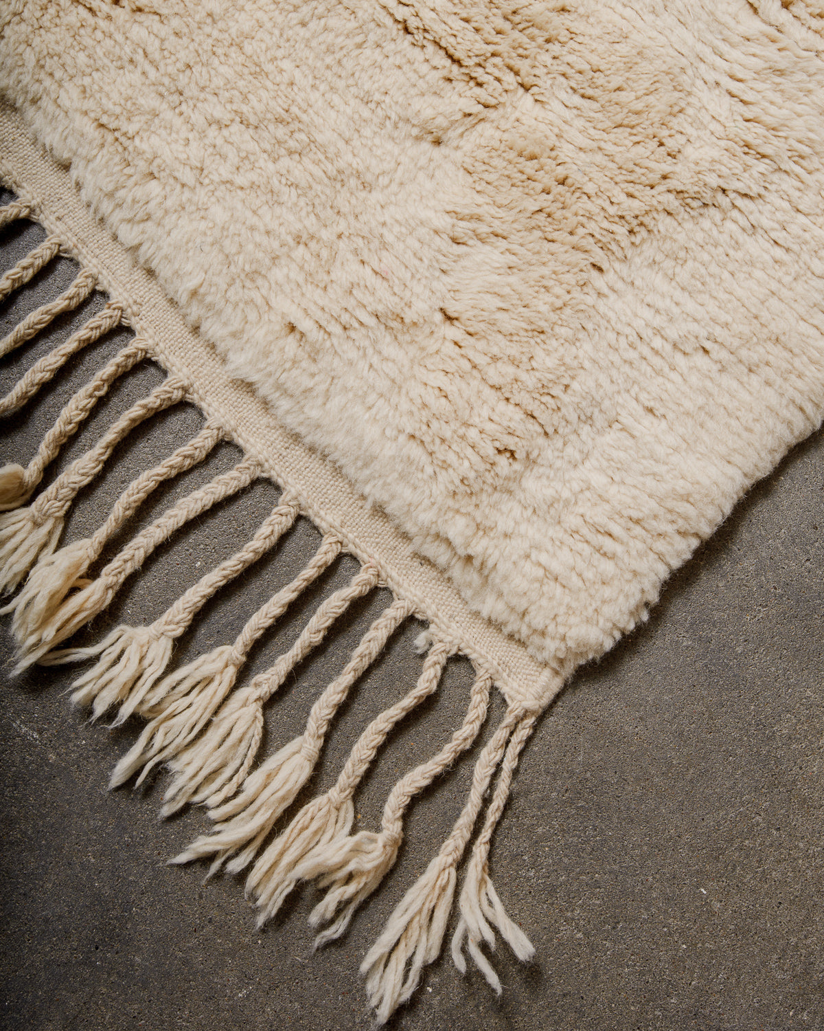 Beige woven rug with fringes on a cement surface