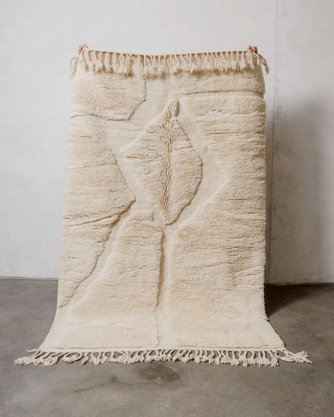 Textured cream wool rug with fringe on a plain background