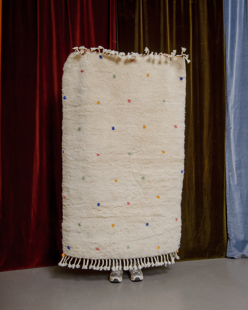 Berberlin Finest dotted rug being held up in front of velvet curtains. 