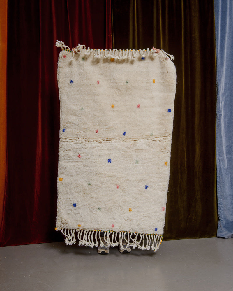 Berberlin Finest dotted rug being held up in front of velvet curtains. 