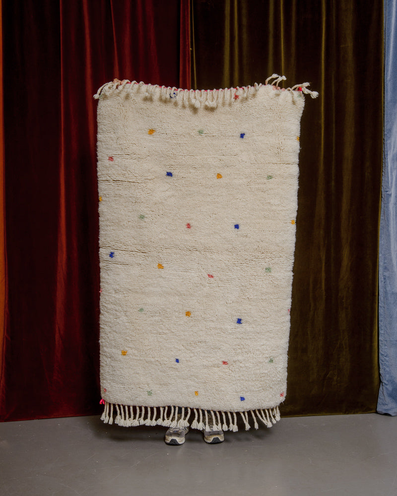 Berberlin Finest dotted rug being held up in front of velvet curtains. 