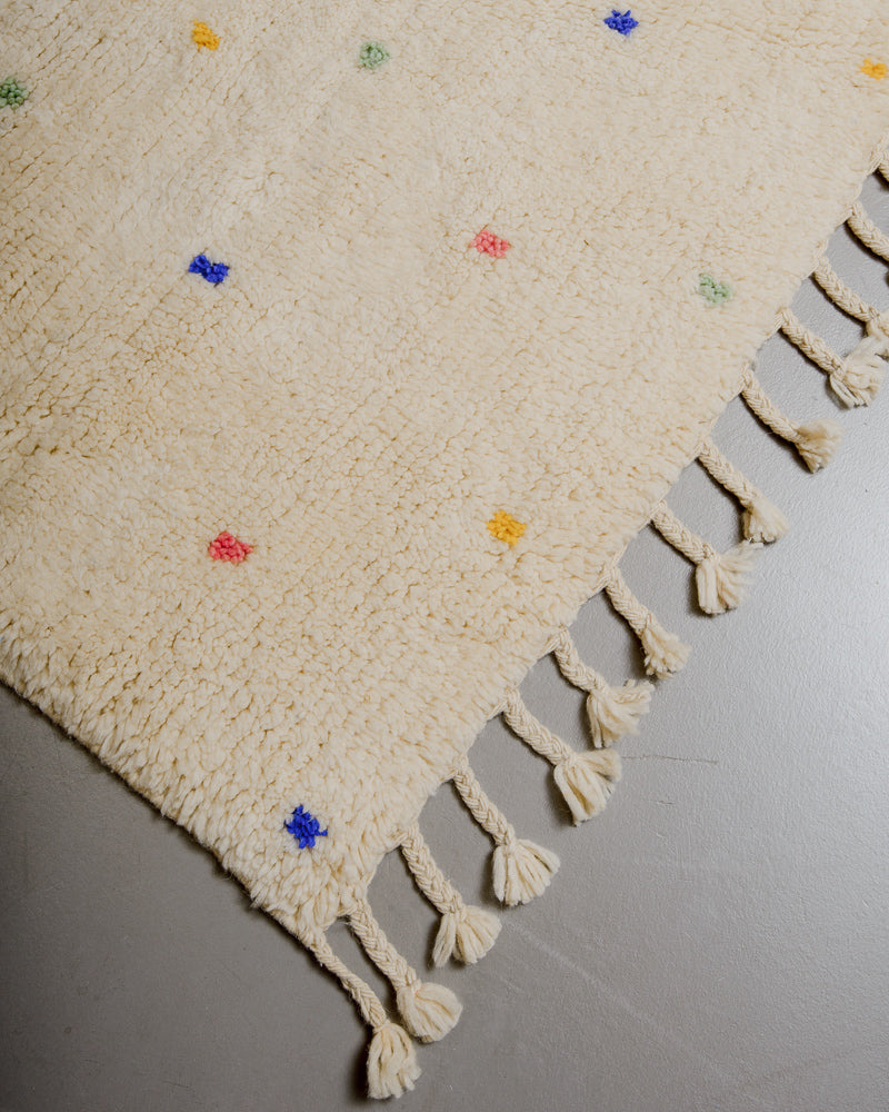 Corner of cream wool rug with colourful polka dots and natural wool tassels.