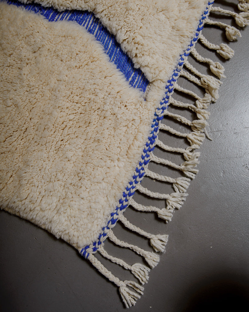 Corner of wool rug with tassels on grey floor. 