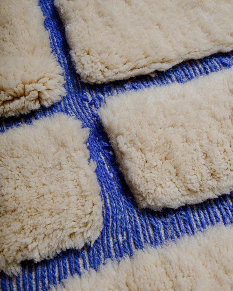 Close up of rug made of fluffy cream wool pile and woven blue lines.