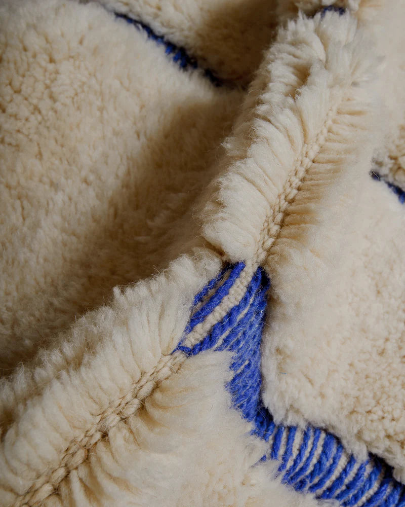 Close up of rug made of fluffy cream wool pile and woven blue lines.